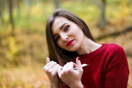 Portrait of beautiful young brunette girl reading a book in the park at fall.の写真素材