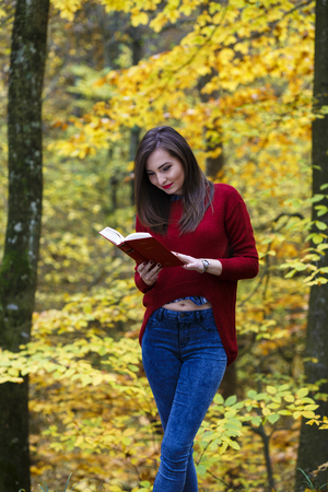 Portrait of beautiful young brunette girl reading a book in the park at fall.の写真素材