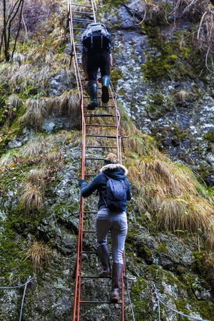 couple of hikers climbing on safety cables in a gorge above the riverの写真素材