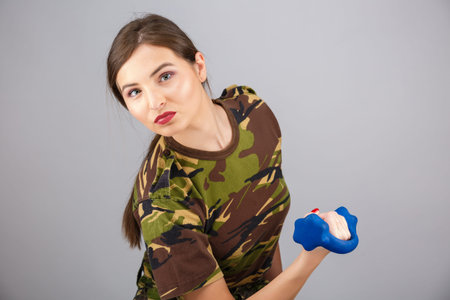 A sporty female fitness model dressed in a military camouflage holds dumbbells.の写真素材