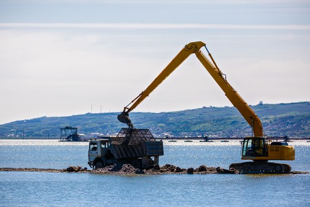 an excavator loads a dump sand in the waterの写真素材