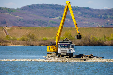 an excavator loads a dump sand in the water