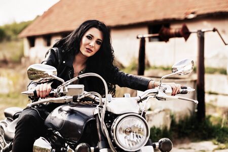 Beautiful motorcycle brunette woman with a classic motorcycle (cinema bleach bypass effect)の写真素材