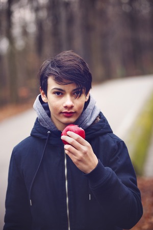young man eating a red apple in the parkの写真素材