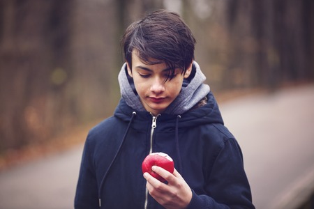 young man eating a red apple in the parkの写真素材