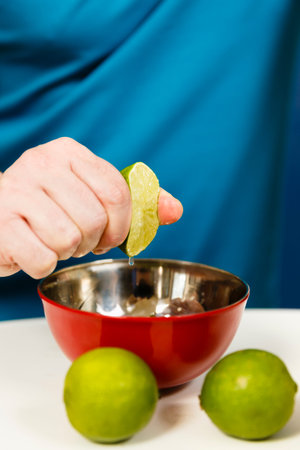 Man squeezing half a lime into a bowl, selective focus