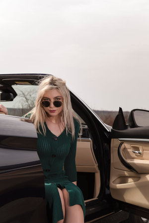 Attractive young woman posing leaning on convertible car