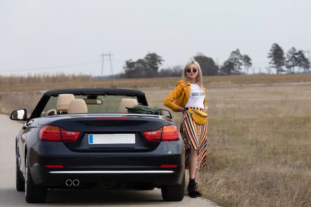 Attractive young woman posing leaning on convertible car