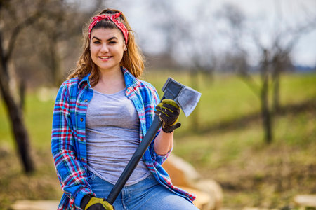 young woman with an ax in her hand rests after breaking beech logs.