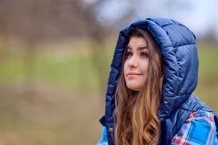 portrait of a young woman wearing a hooded jacket with nature in the backgroundの写真素材