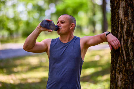 Stay hydrated. Sporty Caucasian drinking water from plastic bottle after his training at park.の写真素材