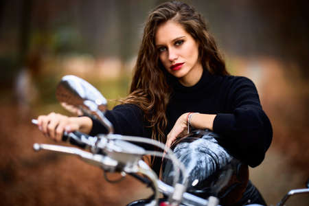A beautiful woman with long hair on a chopper motorcycle in autumn landscape.の写真素材