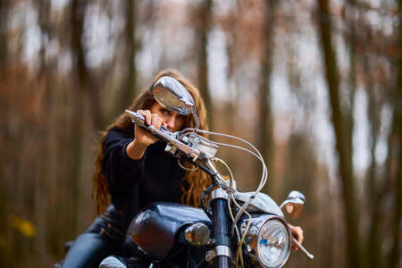 A beautiful woman with long hair on a chopper motorcycle in autumn landscape.の写真素材