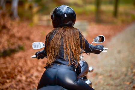 A beautiful woman with long hair on a chopper motorcycle in autumn landscape.の写真素材