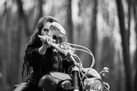 A beautiful woman with long hair on a chopper motorcycle in autumn landscape.の写真素材