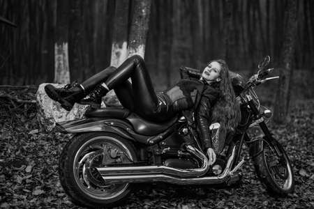 A beautiful woman with long hair on a chopper motorcycle in autumn landscape.の写真素材