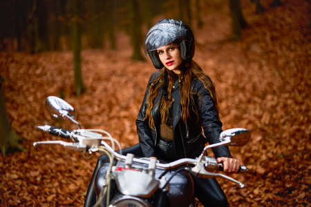 A beautiful woman with long hair on a chopper motorcycle in autumn landscape.の写真素材