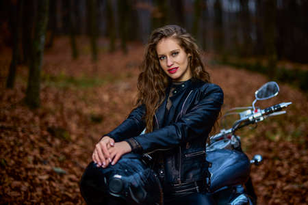 A beautiful woman with long hair on a chopper motorcycle in autumn landscape.の写真素材