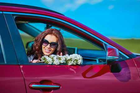 portrait of a beautiful woman in a car holding flowers in her hand.