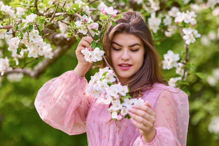 a young woman in a pink dress posing next to a blossoming apple, spring portrait.の写真素材