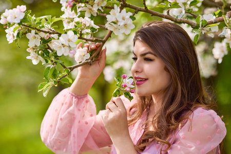 a young woman in a pink dress posing next to a blossoming apple, spring portrait.