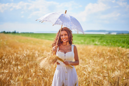 A beautiful woman on a sunny day with an umbrella in a field.の写真素材