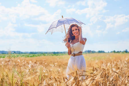 A beautiful woman on a sunny day with an umbrella in a field.の写真素材