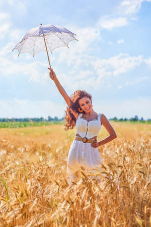 A beautiful woman on a sunny day with an umbrella in a field.の写真素材
