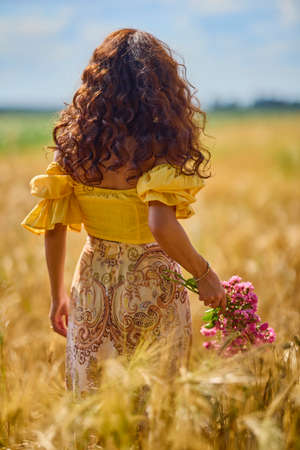 A young and beautiful Caucasian woman happy with a bouquet of flowers in a field.の写真素材
