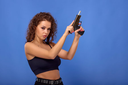 beautiful young woman with curly hair with a gun on a blue background