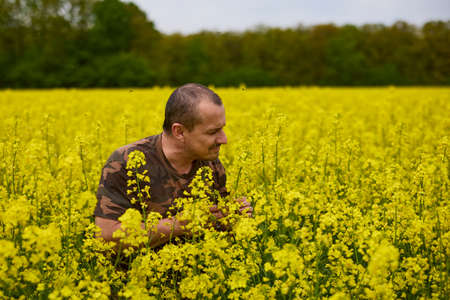Farmer in camouflage clothes in a field of flowering rapeseedの写真素材