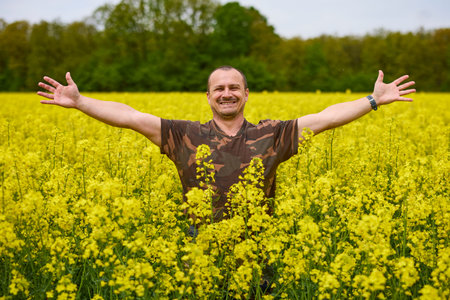 Farmer in camouflage clothes in a field of flowering rapeseed
