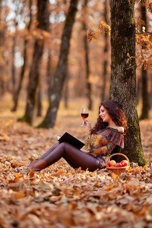 the beautiful woman is reading a book with a glass of wine in her hand during autumnの写真素材