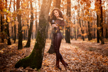 Portrait of a beautiful woman in the forest on a sunny autumn day with a glass of red wineの写真素材