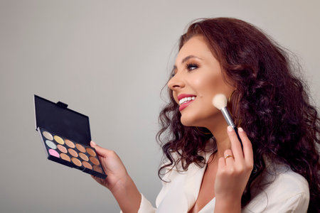 portrait of a beautiful woman with makeup tools in her hand on a gray background.の写真素材