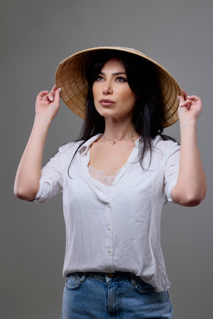 Portrait of a beautiful brunette woman with a Vietnamese hat posing in the studio.の写真素材