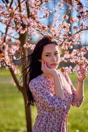 portrait of a beautiful woman posing by a blooming tree on a sunny spring day.の写真素材