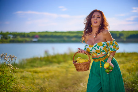 portrait of a beautiful woman with lemons on a meadow near a lake.の写真素材