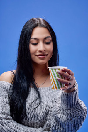 Portrait of a beautiful young brunette posing in the studio on a blue background with a cup of...