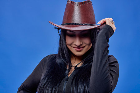 a young brunette with long hair and a hat posing in the studio isolated on a blue background.の写真素材