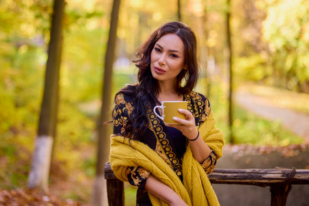 the beautiful brunette a blanket and a cup in the forest during autumnの写真素材