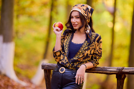 a beautiful woman with a headscarf and an apple in her hand autumn background.の写真素材