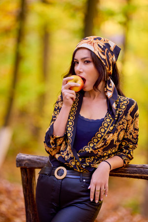 a beautiful woman with a headscarf and an apple in her hand autumn background.の写真素材