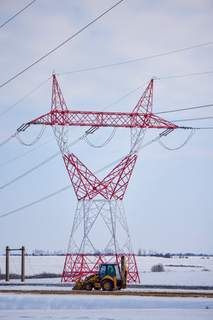 a high-voltage pole in winter with a machine at the baseの写真素材