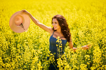 beautiful woman with a hat posing in the blooming rapeseed field on a sunny day