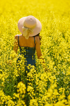 beautiful woman with a hat posing in the blooming rapeseed field on a sunny day