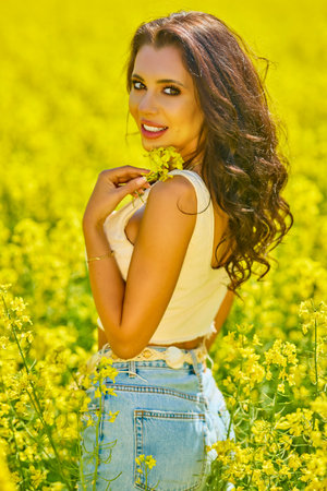 Portrait of a beautiful woman with long hair in a blouse and jeans in a field of blooming rapeseed