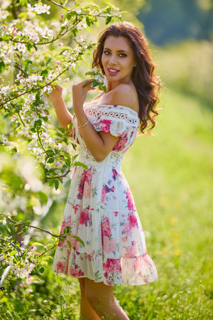portrait of a beautiful woman in a dress in a blooming apple orchard enjoying a sunny spring dayの写真素材