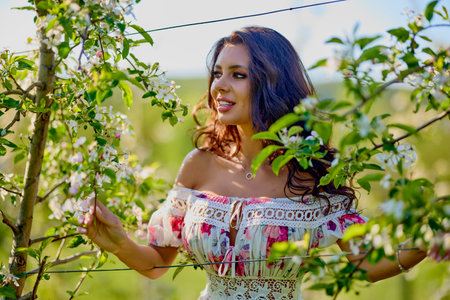 portrait of a beautiful woman in a dress in a blooming apple orchard enjoying a sunny spring dayの写真素材