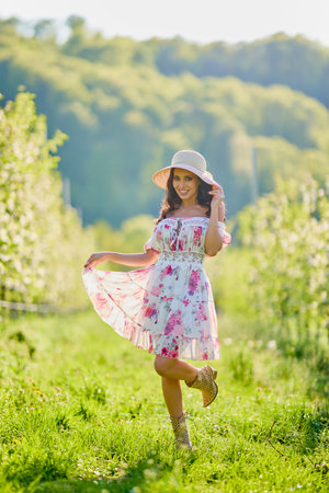 Full body portrait of a beautiful woman in a dress in a blooming apple orchard on a sunny spring dayの写真素材